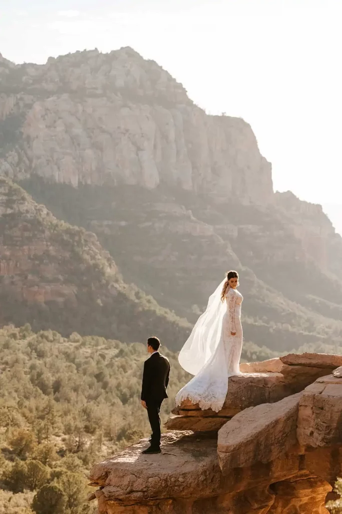the bride stands tall, looking down behind her at her groom; the groom looks out at Sedona's mountains.