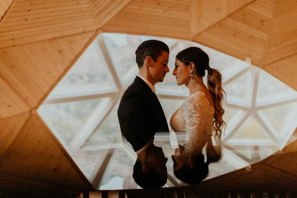 A bride and groom stand together in front of an interesting window.