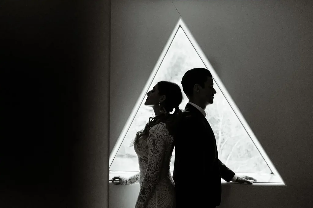 A black and white photograph of a bride and groom standing back to back.