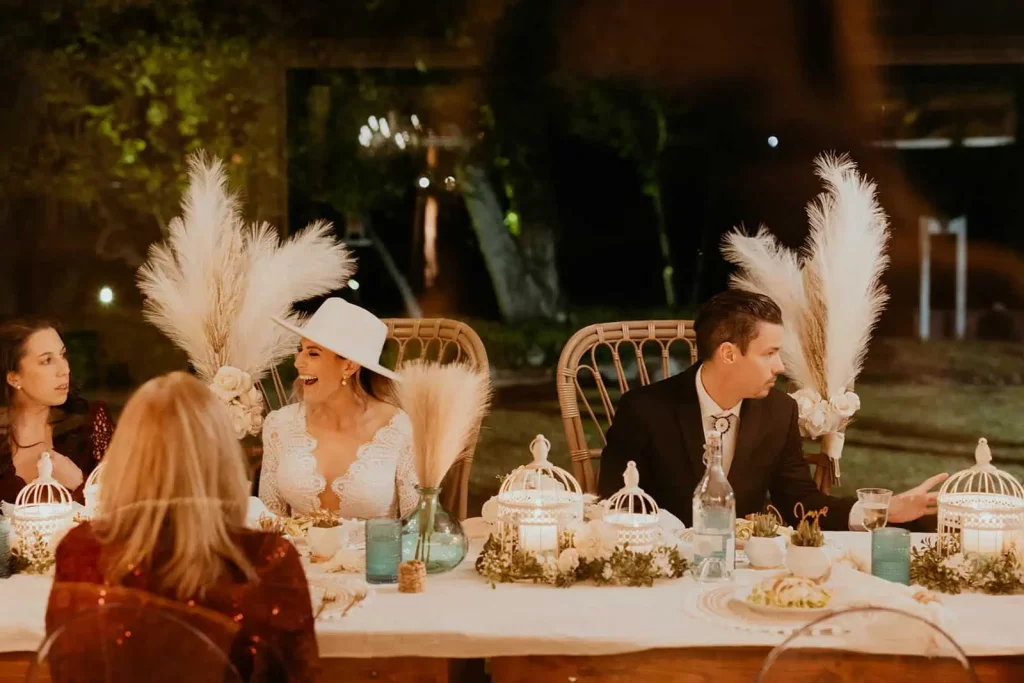 The bride and groom laugh together while sitting at dinner with their guests.