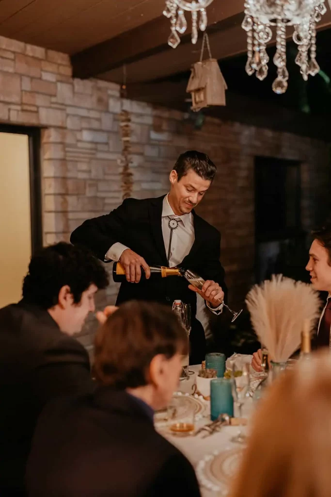 A groom pours champagne in this candid photograph at dinner.