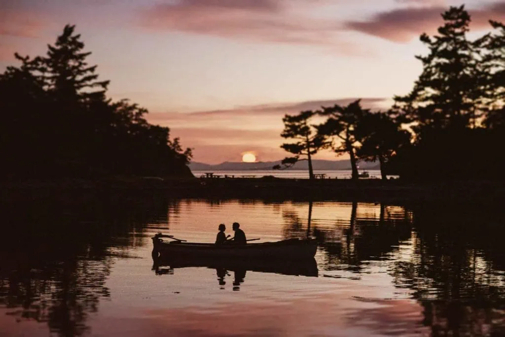 a couple looking at each other on kayak, with the sun setting in the background and everything cast in shadows