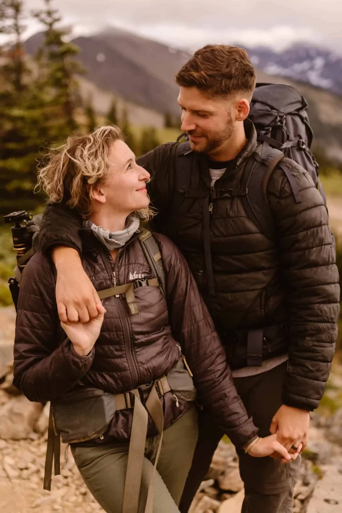 A man and woman smile while looking at each other with all of their adventure gear ready to go.