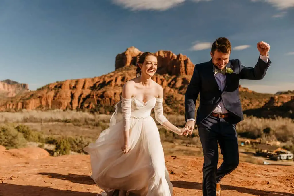 A bride and groom walk together back down the aisle and celebrate and smile as they go in Sedona.