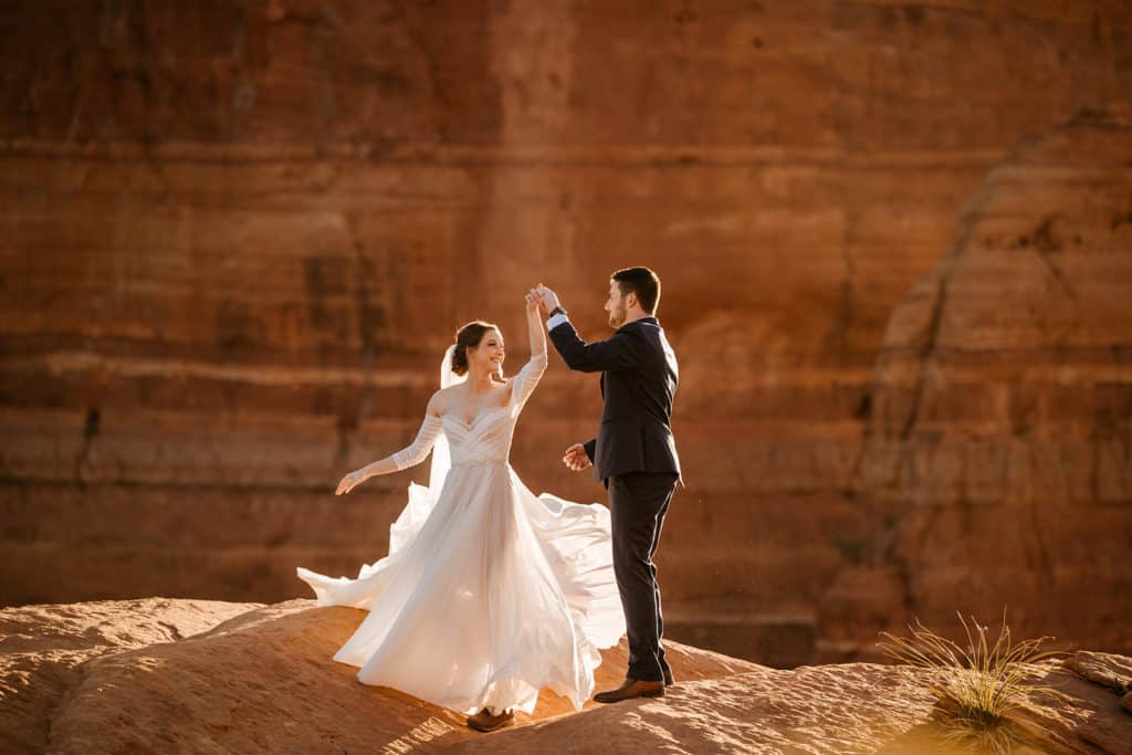 a groom twirls his bride, letting her dress flow in the air. they're smiling in front of sedona's red rocks