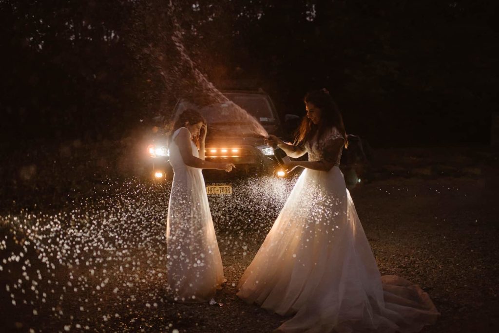 Two brides celebrate their elopement in Washington by spraying champagne in front of their car.