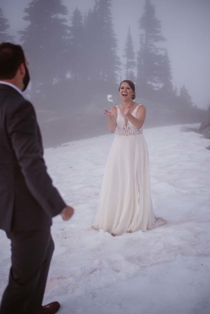 a bride and groom throwing snow back and forth to one another.