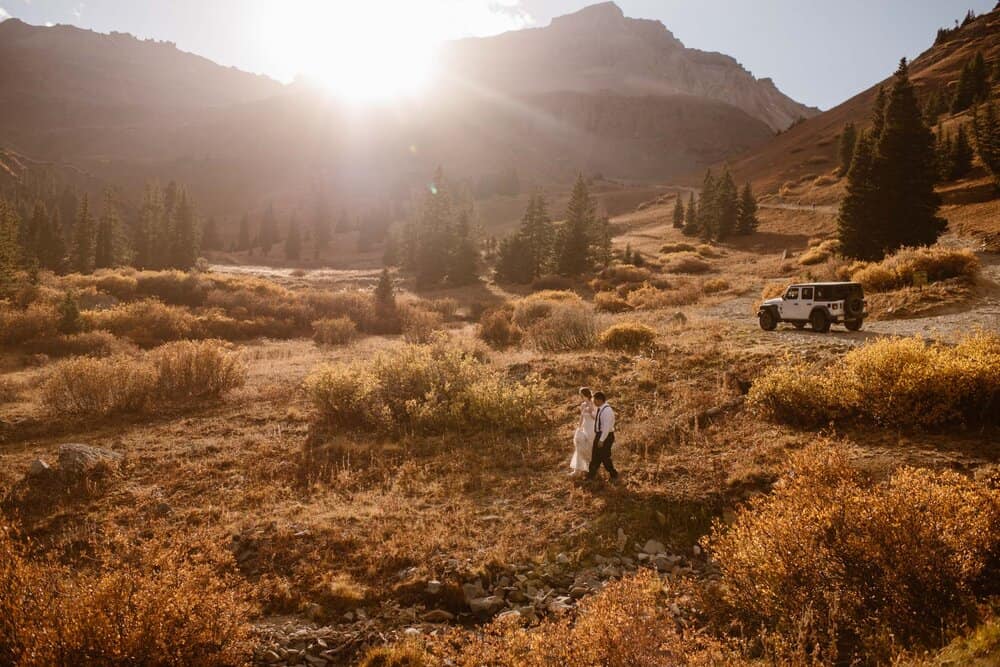 a couple walking through ouray Colorado's landscape, jeep in the background and sun shining from the mountains.