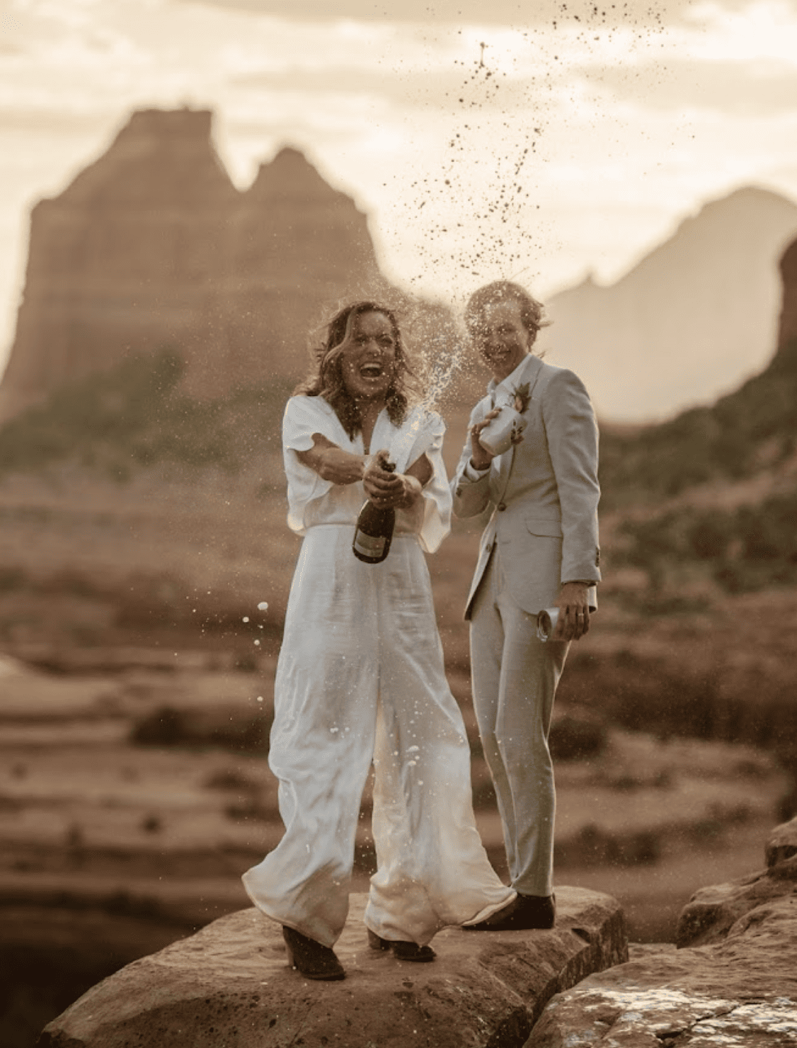 Two brides spray champgane in celebration of their marriage on top of a vista in Sedona.