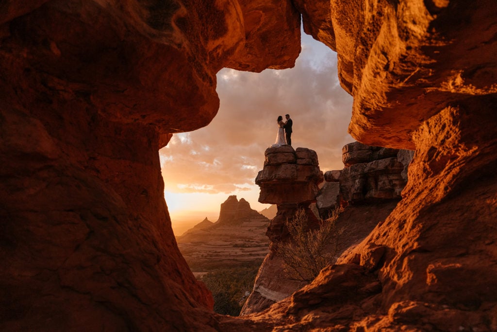 a couple embracing on top of a rock, seen through a hole in the rocks of Sedona's canyons.