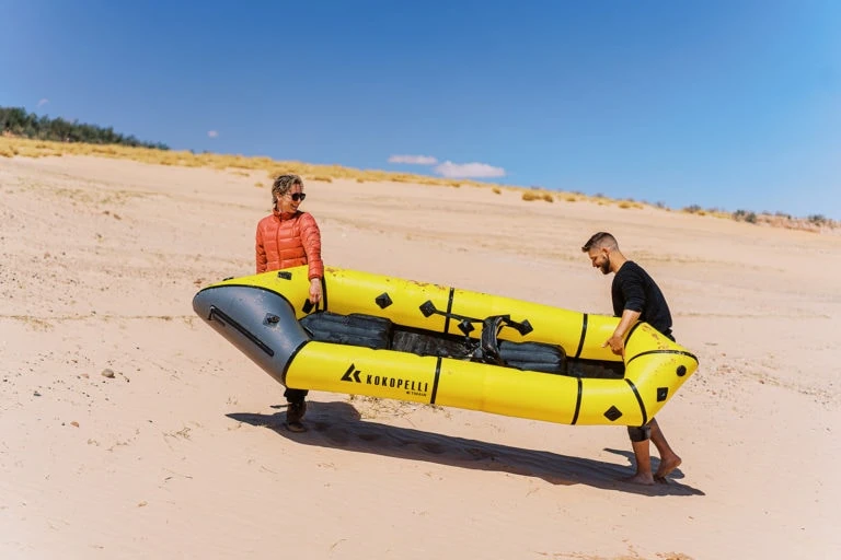 couple carrying life raft up beach.