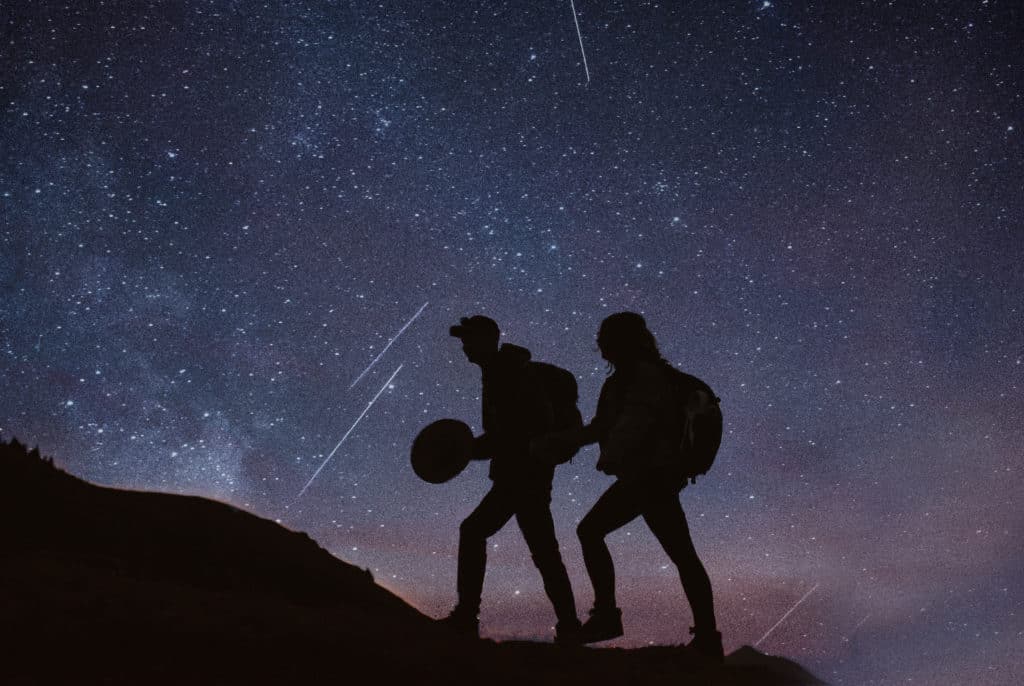 A silhouette of a couple hiking together with the stars filling the sky behind them. 