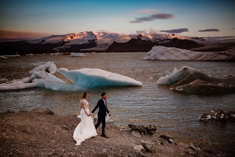 a bride and groom walking along the shoreline, looking at Iceland's water and glaciers.