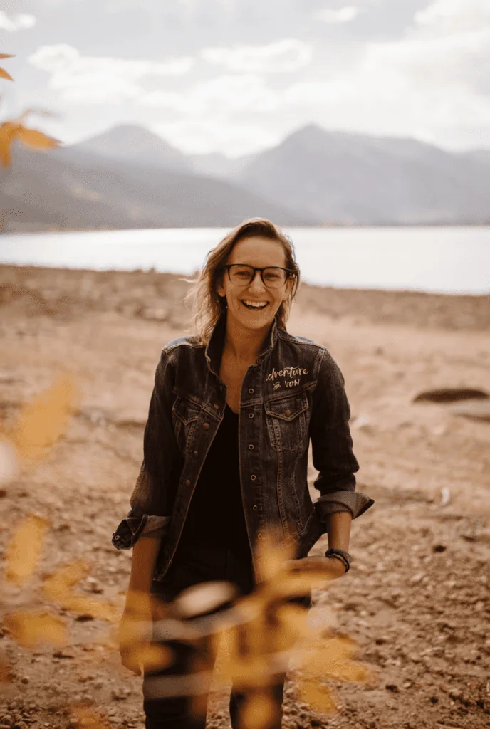 A person smiles with a lake and mountains behind them in this portrait.