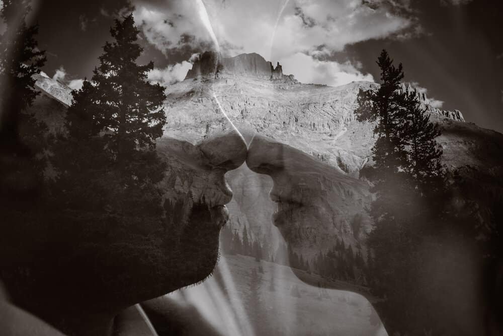 A double exposure of a couple going to share a kiss and the mountains in the background.