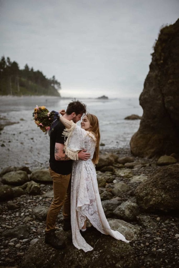 A couple holds each other on ocean shores on a moody pnw day during their elopement.  