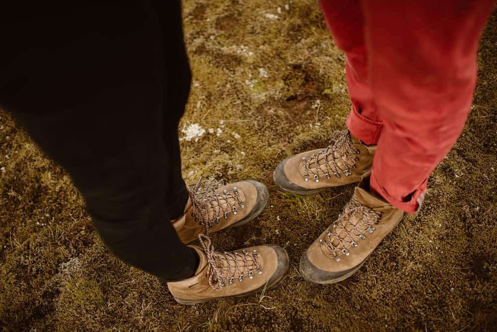 A couples pair of hiking boots on their feet as they stand on moss. 