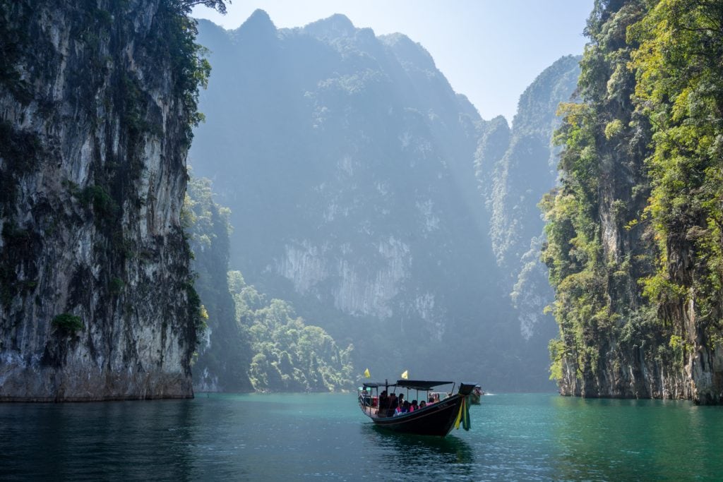 A boat in the waters of Thailand surrounded by large mountain peaks.
