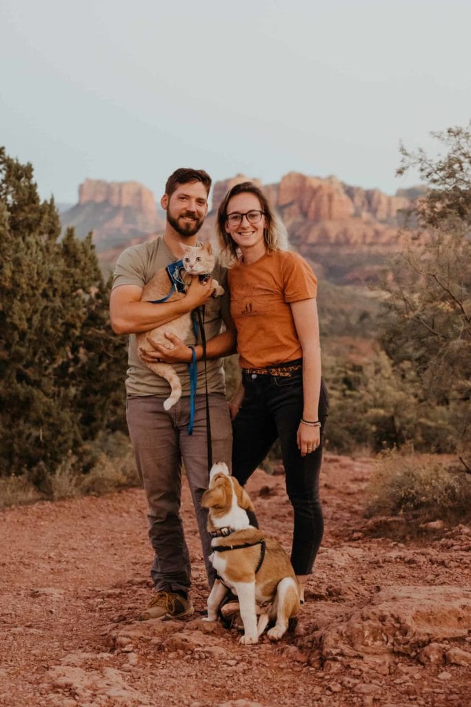 An elopement photography team stand for a portrait together with their cat and dog. 