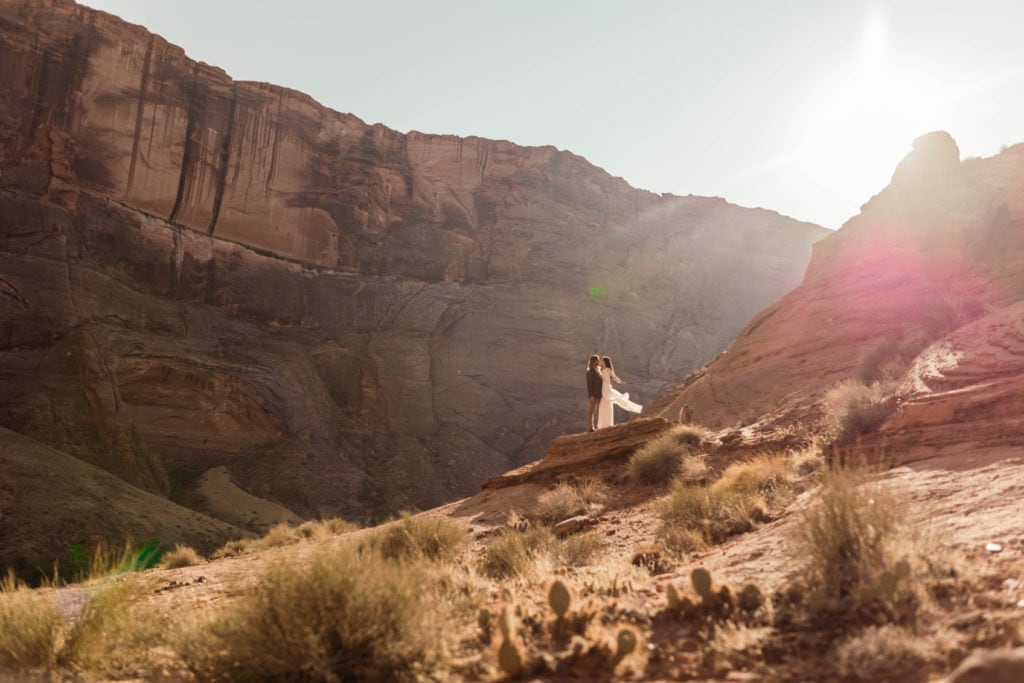 A couple stand facing each other while down in a canyon and the wind catches the brides dress. 