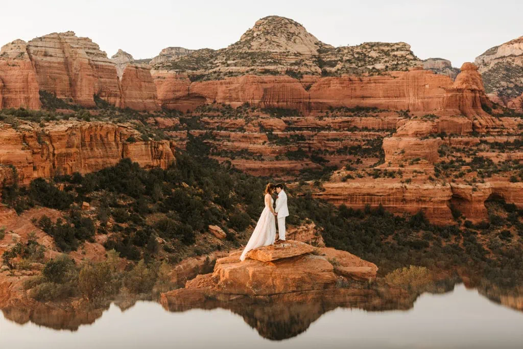 Two brides face each other holding hands surrounded by red rock canyons in sedona. 
