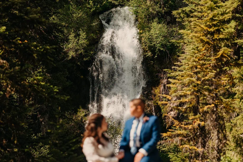 A waterfall flows behind the couple as they sit and talk with each other. 