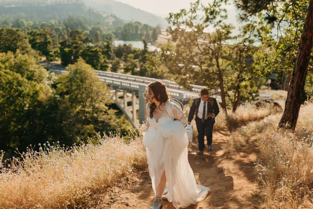 The brides walk up the hill at the start of the trail with a bridge in the back ground. 