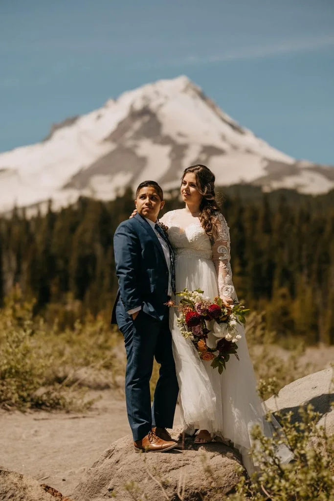 The wedding couple looks out towards the mountains with Mt Hood behind them on a sunny day. 