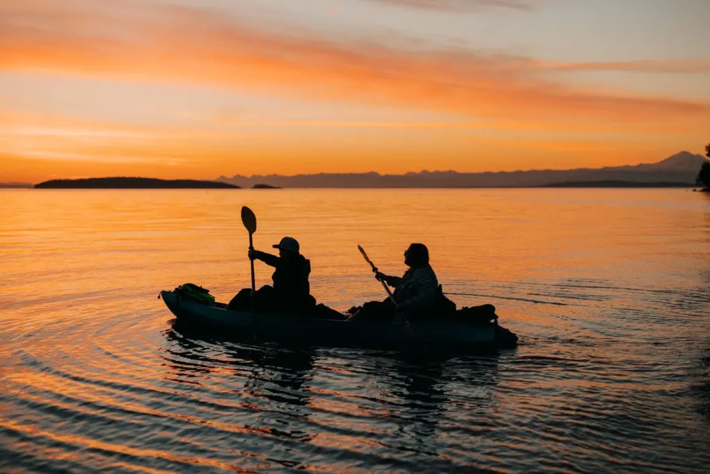 the bride and groom kayak, sending ripples around, in the orange sunset.