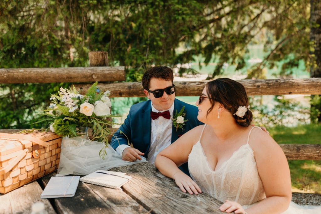 A bride and groom sitting together on a picnic table.