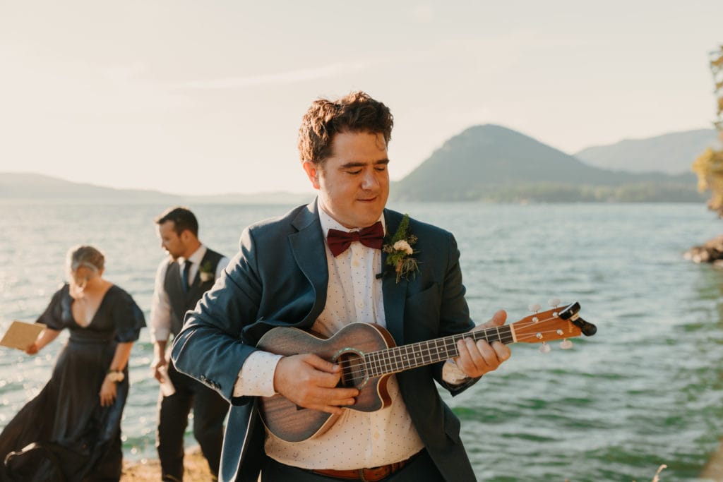 A groom playing ukulele as his bride walks down the aisle.