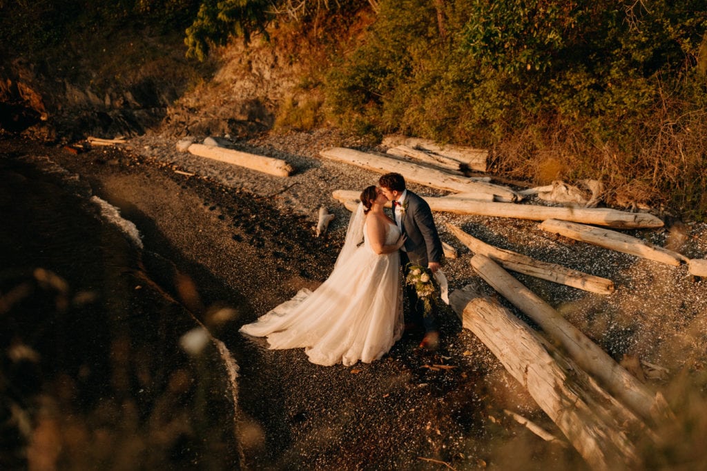 A bride and groom share a kiss on the shore
