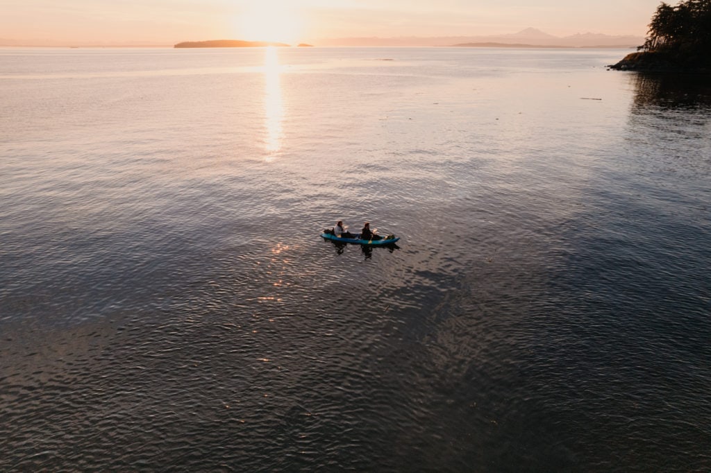 A drone image of a couple kayaking together on the ocean at sunrise