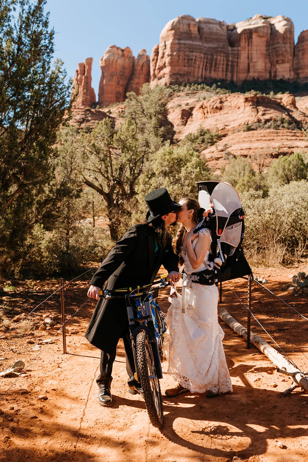 A couple shares a kiss as they leave Cathedral Rock after their mountain biking elopement with their son in tow.