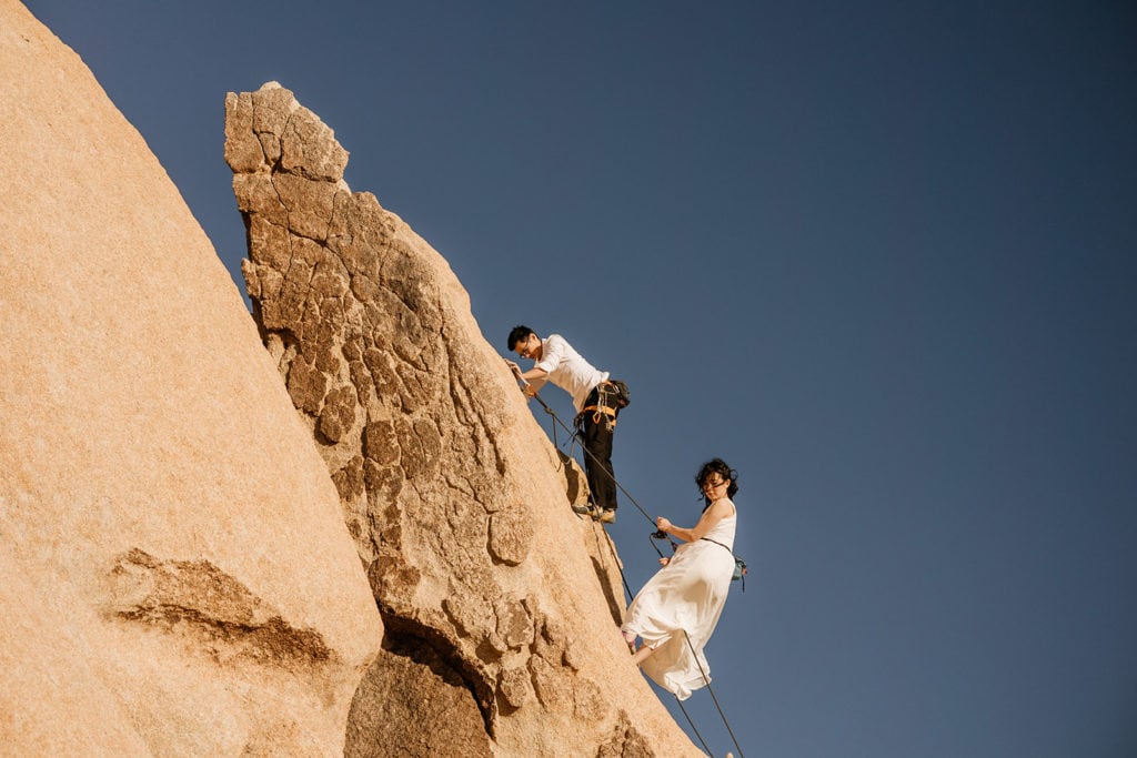 A couple raps down a climbing route together in their wedding attire. 