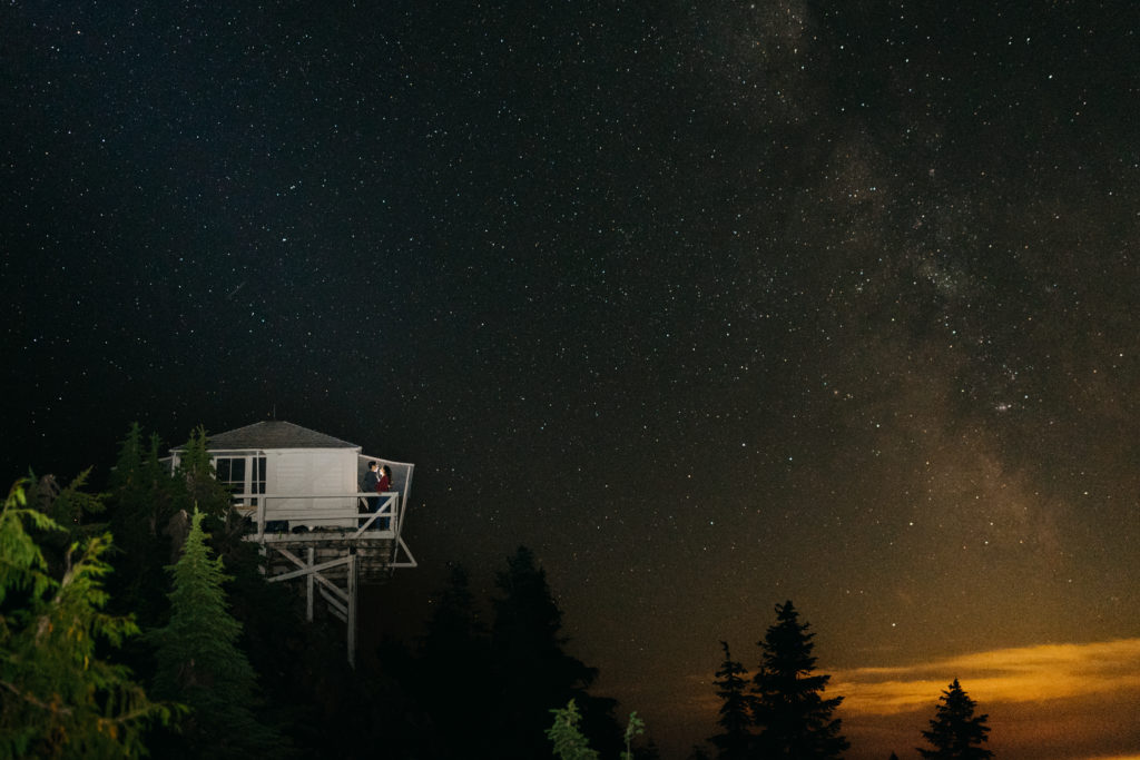 The milky way over the fire tower on a summer night as a couple camps on the towers deck. 
