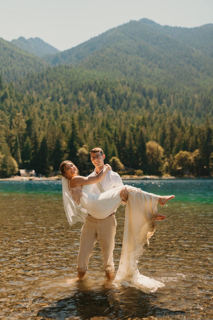 A groom holds a bride as they cool off in lake crescent together. 