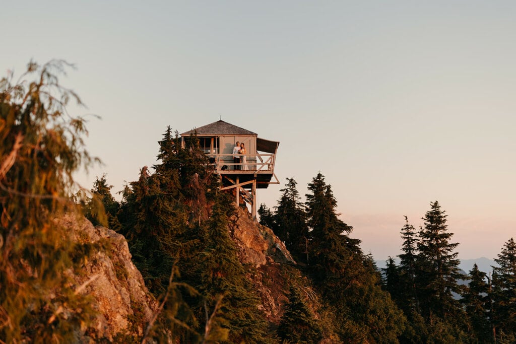 A couple stands on the balcony of a fire tower in the Mount Baker Wilderness. 