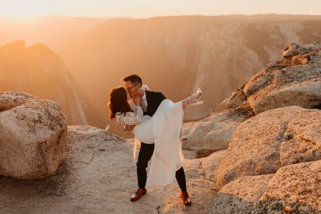A groom picks up and kisses his bride in the sunset light. 