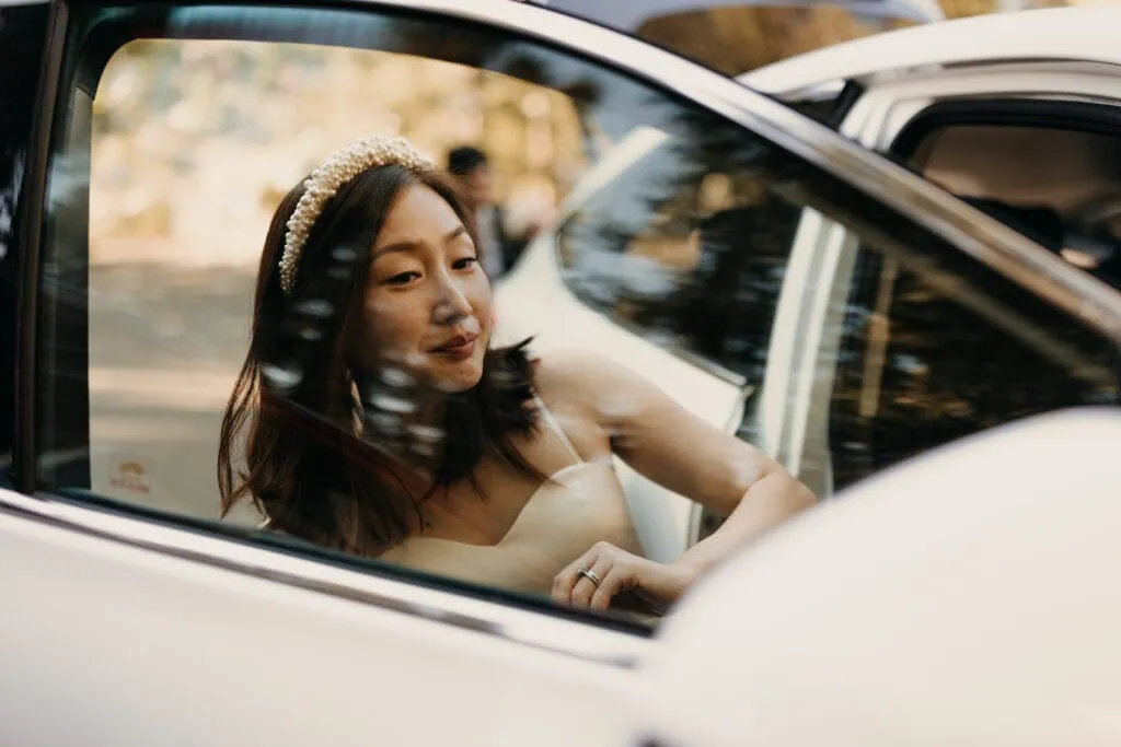 A bride gets ready for her ceremony by her car mirror. 
