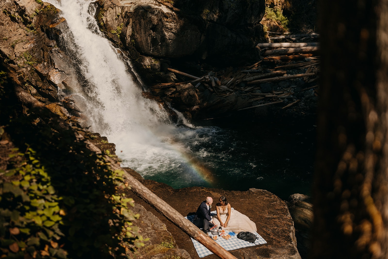 A couple sits together at a waterfall having a picnic.
