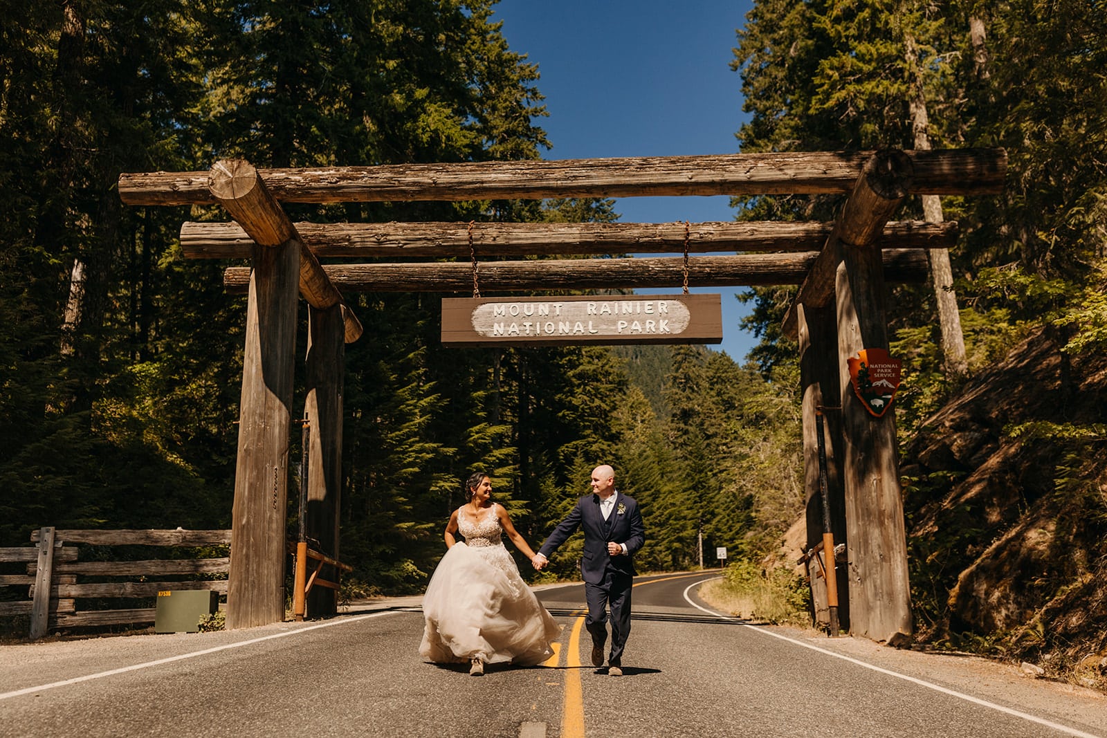 A couple runs under the Mt Rainier National Park Sign together.
