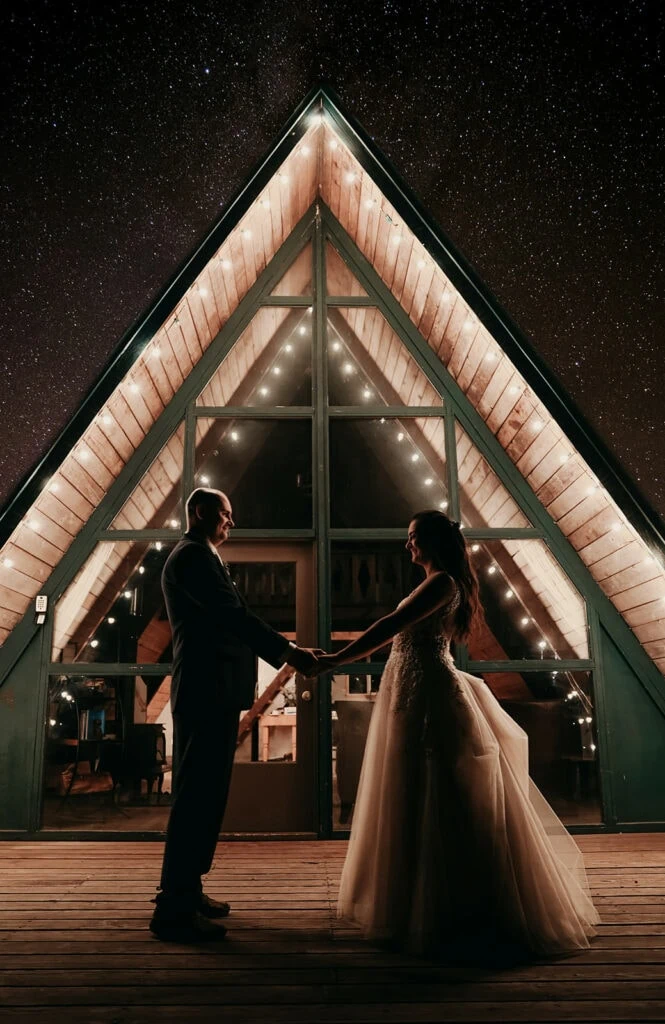 The couple stands on the cabin deck at night under the stars.