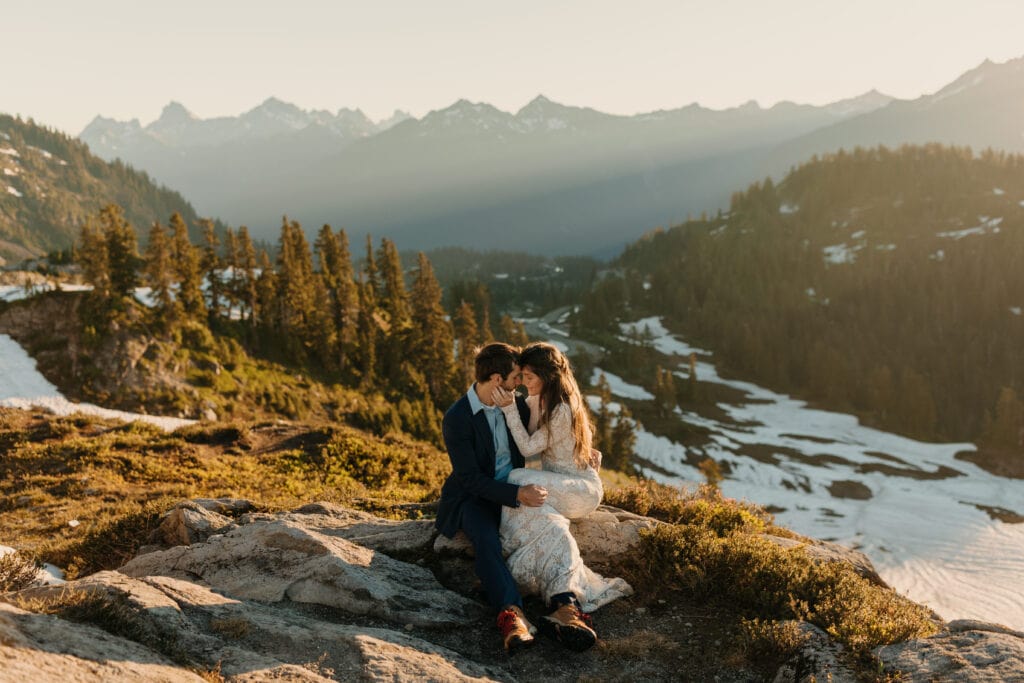 A couple sits together holding each other at sunrise in the mountains for their elopement day at artist point. 