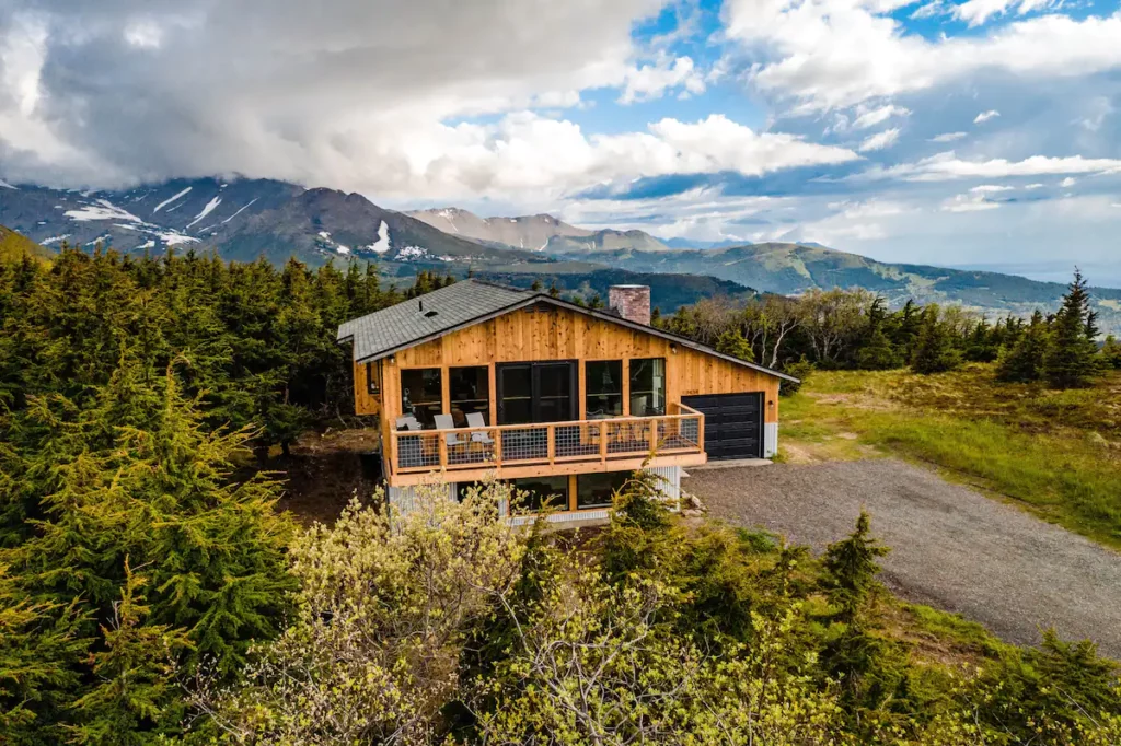 A modern cabin sits in view of the mountains of Alaska. 
