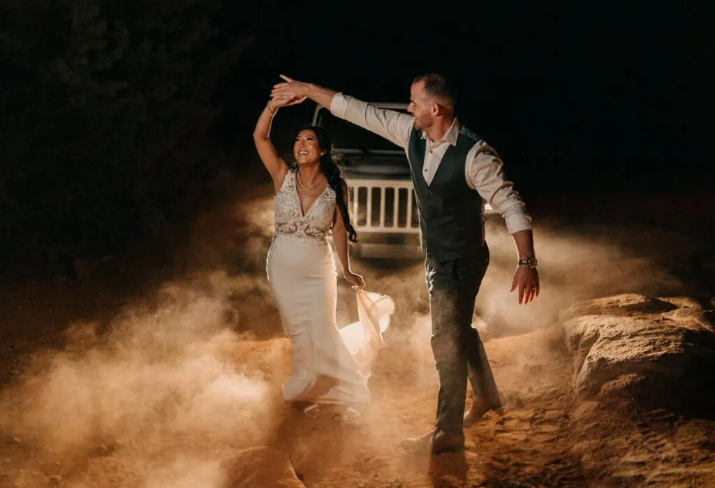 A couple shares their first dance in front of their jeep headlights.