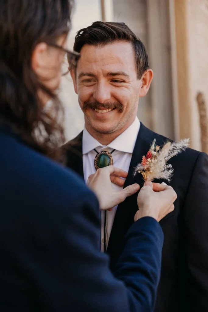 A man helps put a boutonniere on the groom.