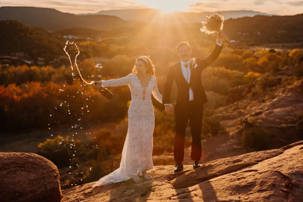 A bride and groom pop a bottle of champagne to celebrate their wedding day at sunset in Sedona