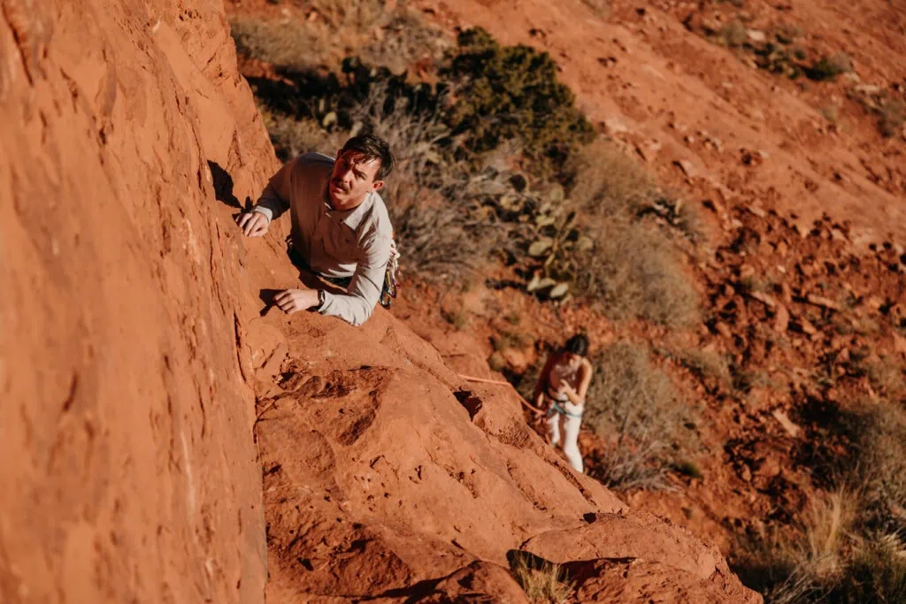 A groom looks up to continue his climb up this Sedona climbing route as his bride belays him