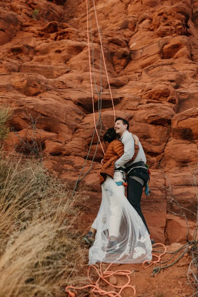 A bride and groom embrace for a hug as the just finished their rappel down to the base of their sedona climb.